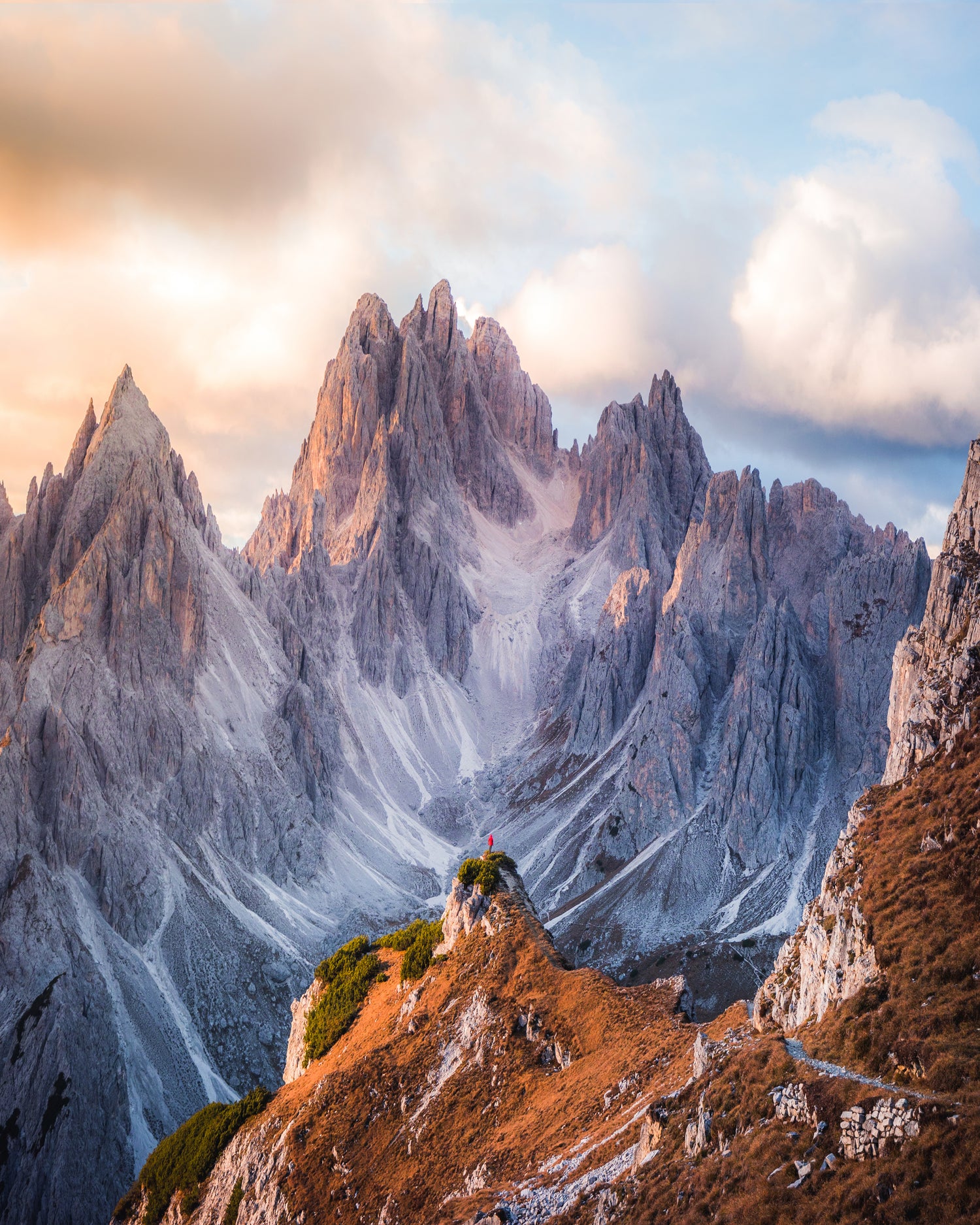 A hiker stands in awe, looking up at the vertical mountain peaks of the Dolomites, bathed in the golden light of sunset.