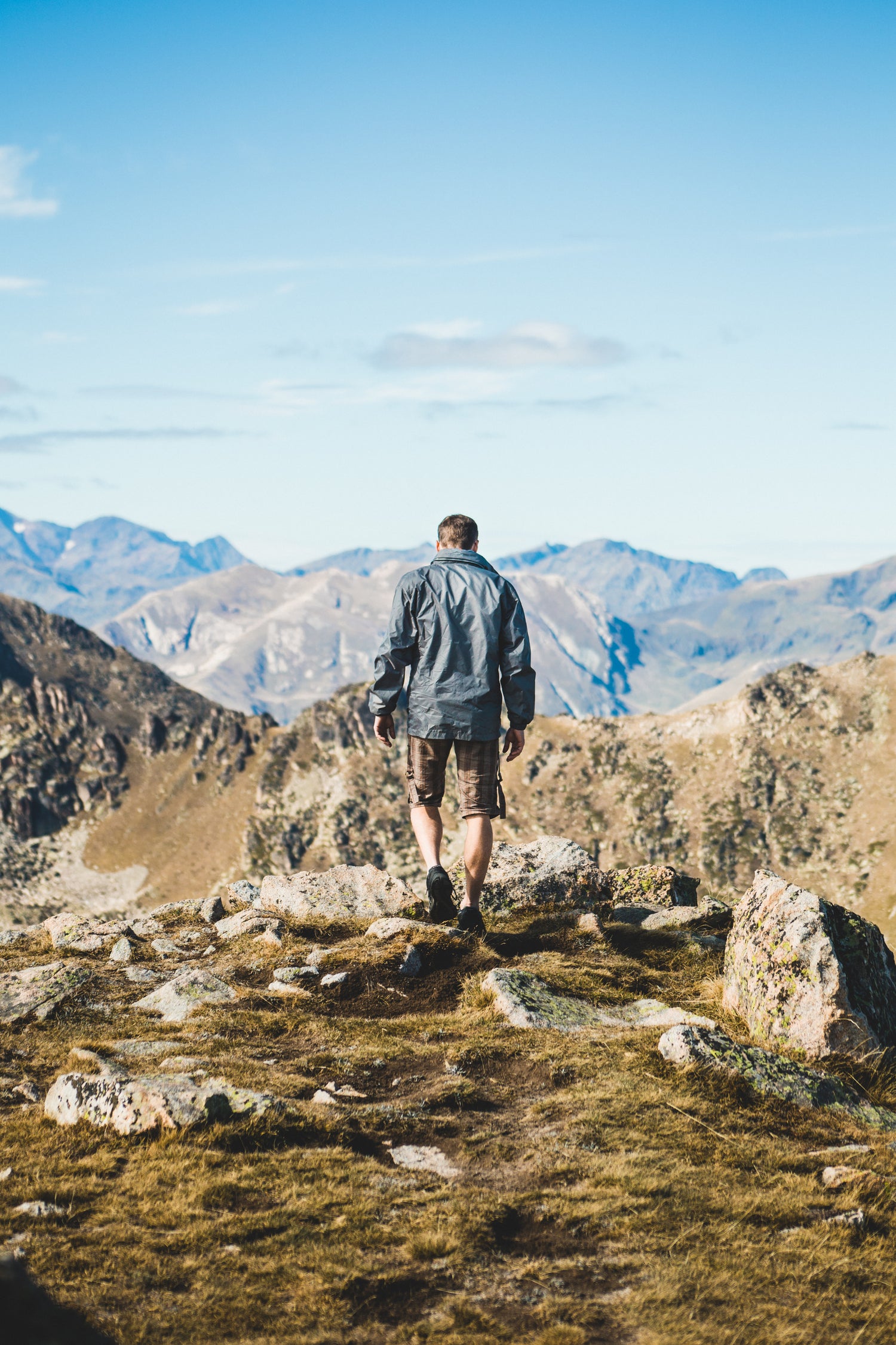 A man hiking in mountains, confidently walking along a rugged mountain top, surrounded by breathtaking scenery.