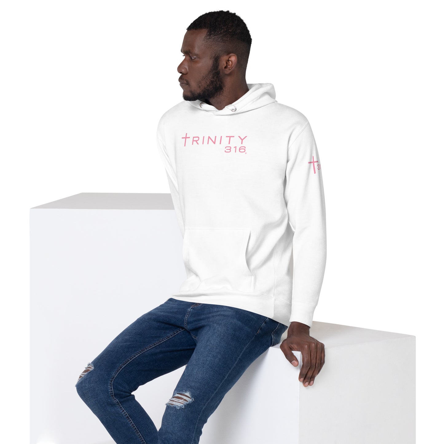 A man wearing a white hoodie with pink text sits on a white box, presenting a modern and trendy appearance.