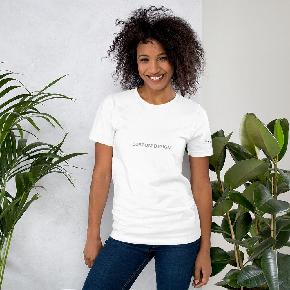 A woman in a white unisex staple t-shirt featuring the words be kind prominently displayed on the front.