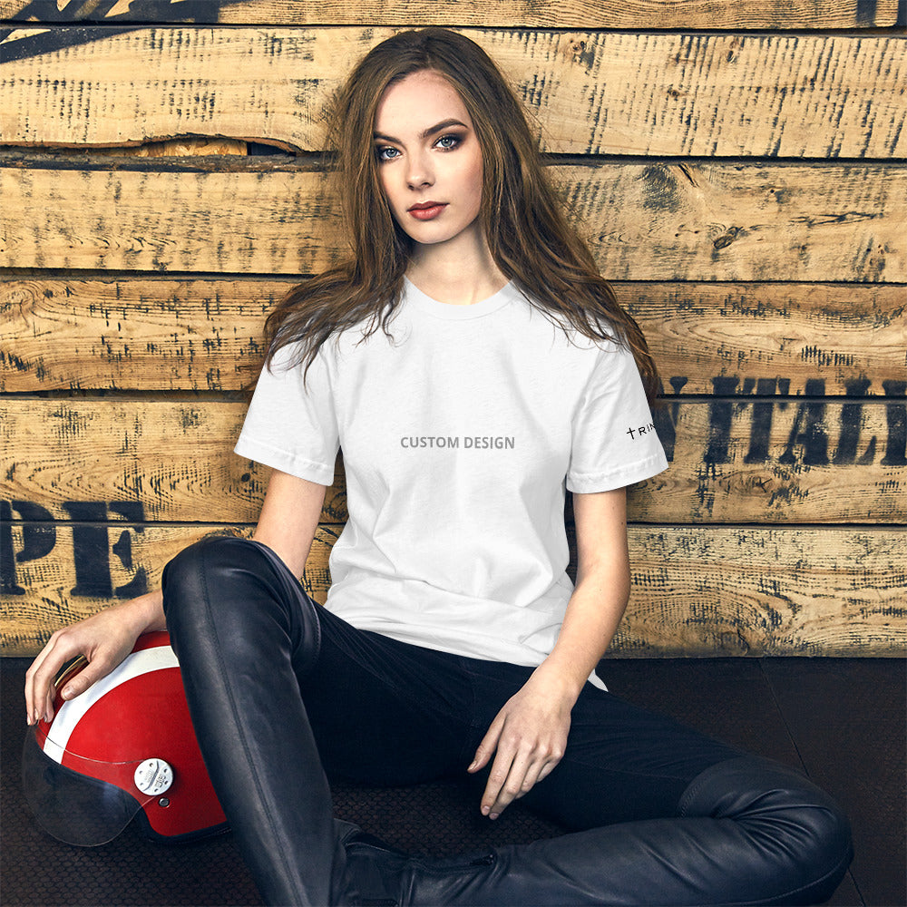 A woman in a unisex staple t-shirt white front and black pants sits gracefully on a wooden wall, enjoying her surroundings.