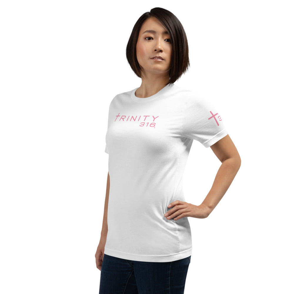 A woman in a unisex staple t-shirt, white with pink lettering, poses confidently, showcasing a casual yet stylish look.