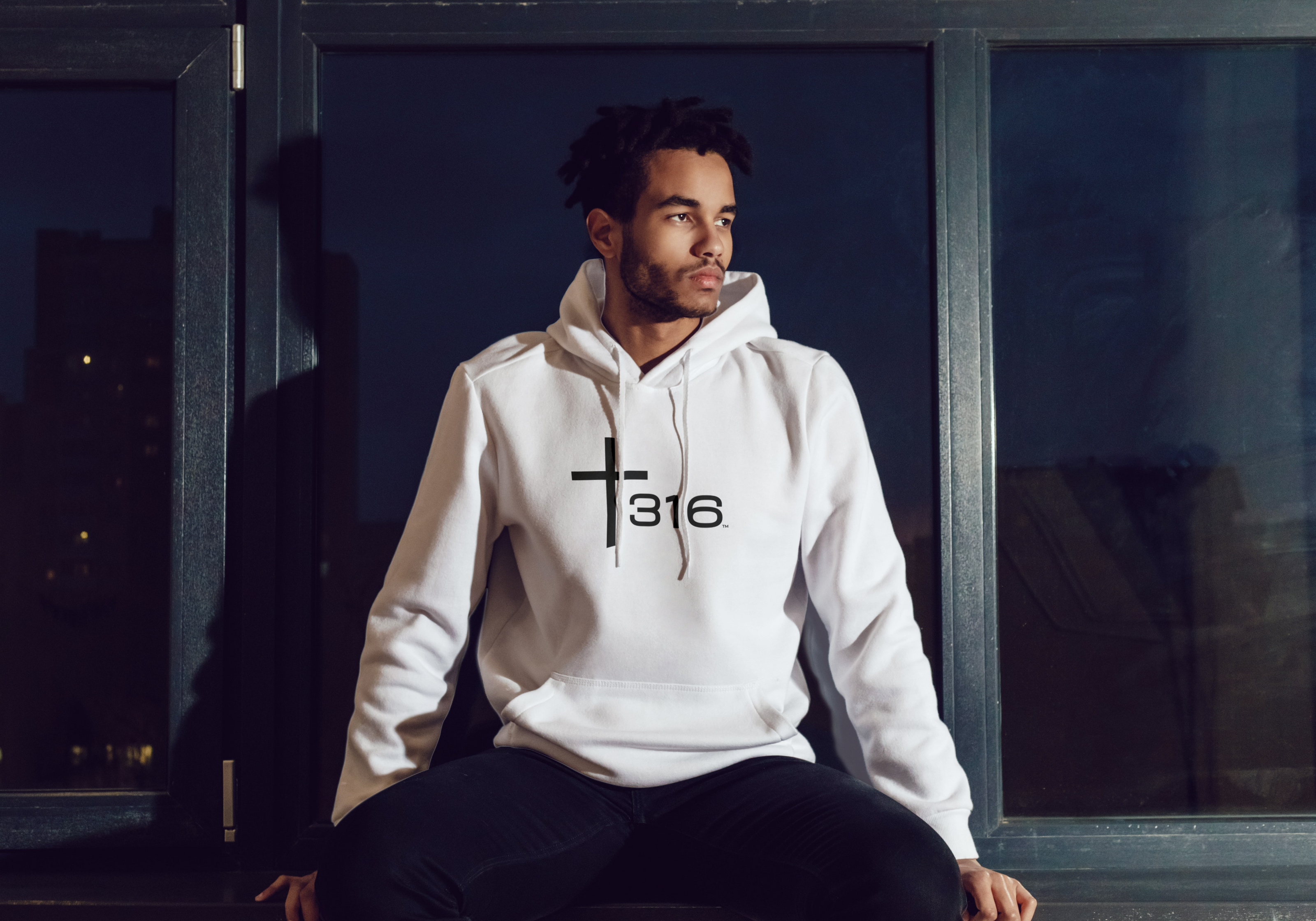 An African American man in a white hoodie sits on a window, with the Trinity 316 logo visible.